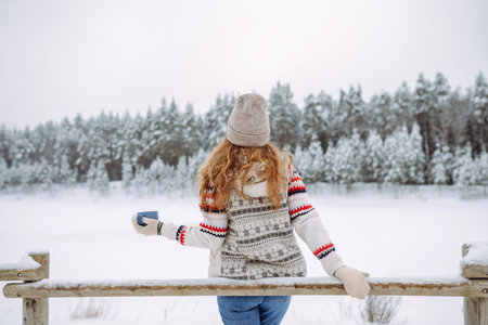 Cute woman drinks a hot drink from a thermos in a winter snowy forest. Winter walk.の写真素材