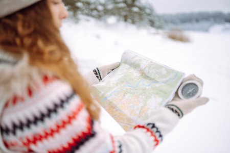 Curly-haired young woman standing in the wild with a map and compass in a snowy forest.の写真素材
