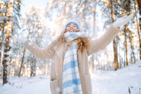 Young woman in warm clothes plays with snow on a sunny winter day. Concept of walking, fun.
