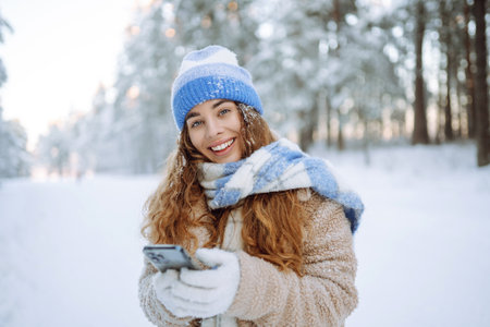 A young woman in a snowy park with a phone in her hands communicates via video and takes a selfie.