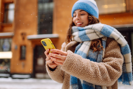 Phone in the hand of young woman in winter street. Online communication. Technology concept.の写真素材