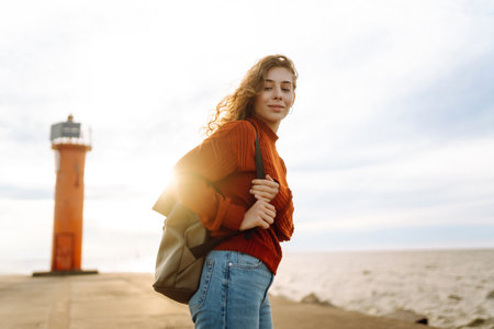 Portrait of woman enjoying a breezy day near a vibrant red lighthouse at sunset. Lifestyle concept.の写真素材