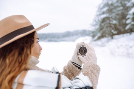 Woman in a hat holding a compass lying in hand on mitten against backdrop of snowy winter forest.