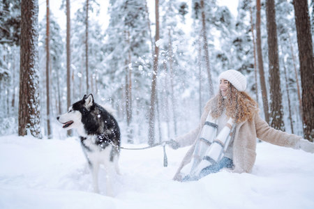 Cute woman spends time with her husky dog in the winter snowy forest. Lifestyle.