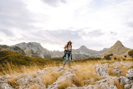 Young woman enjoys sunny afternoon in mountains while sitting on rocks. Tourism. Active lifestyle.の写真素材