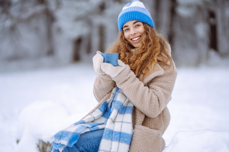 Smiling woman with a thermos in a snowy forest enjoying nature. Adventure concept. Lifestyle.