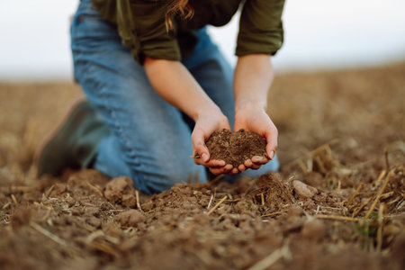 A young woman farmer holds black soil in hand on an agricultural field. Fertility concept, scaling.の写真素材