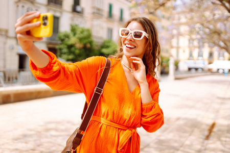 Happy attractive young woman posing to camera make selfie smiling at sunlight on street. Travel