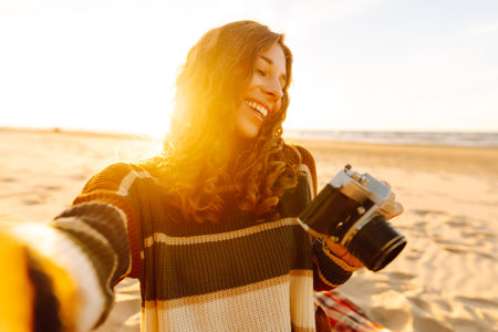 Pretty woman with a professional photographer taking selfie on the beach at sunset. Travel blog.