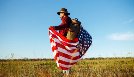4th of July. American Flag. Traveler with the flag of America. The man in a hat, a backpack, a shirt and jeans.の写真素材