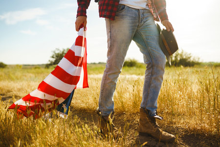 4th of July. American Flag. Traveler with the flag of America. The man in a hat, a backpack, a shirt and jeans.の写真素材