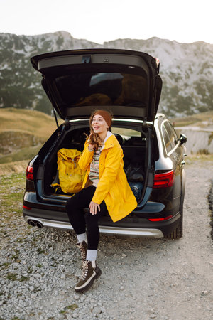 A cheerful traveler enjoying a scenic mountain view while sitting on the trunk. Traveling by car.