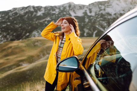 A cheerful traveler enjoying a scenic mountain view while sitting on the trunk. Traveling by car.
