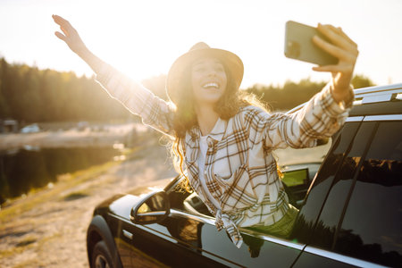 Happy woman on vacation taking selfie photo with smartphone near car. Stylish model on a car trip.