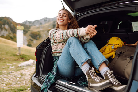 Young woman enjoying autumn nature while sitting in trunk of her car during a solo trip. road trip