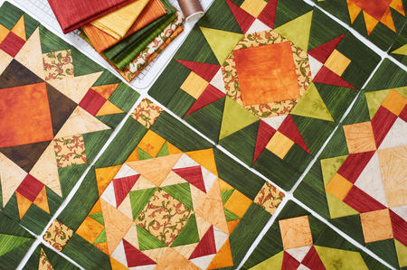 Assembling of quilt from orange-green patchwork blocks, pile of fabricの写真素材