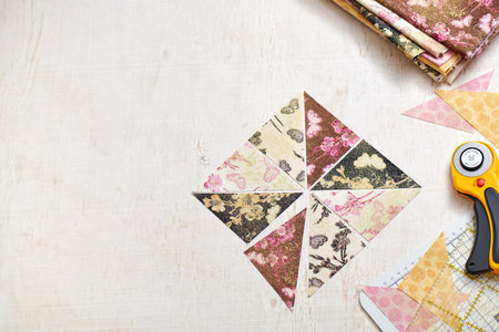 Preparing of triangle pieces of fabrics for sewing quilt block, rotary cutter, rule, craft mat, stack of clothの写真素材