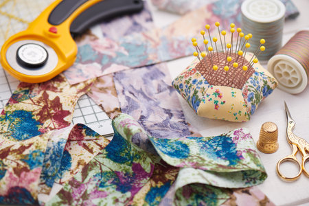 Brightly colored strips of fabric, rotary cutter, pin cushion and quilting accessories on white...