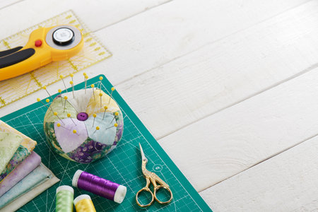 Pincushion, stack of fabrics, sewing and quilting accessories lying on a cutting mat, space for textの写真素材