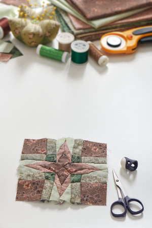 Patchwork block, stack of fabrics, sewing and quilting accessories. Copy space