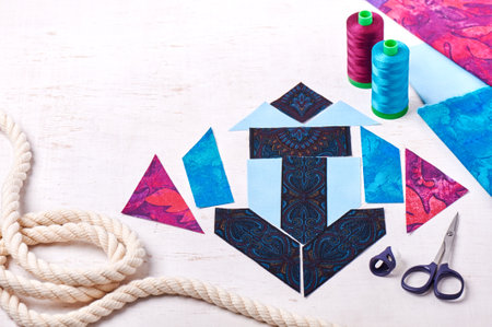Sewing patchwork of block anchor, spools of threads, fabrics, rope lie on white surface