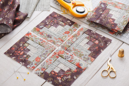 Patchwork log cabin blocks, stack of blocks, sewing accessories on white wooden surface