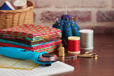 Stack of colorful fabrics on table surrounded by sewing accessories on brick wall backgroundの写真素材