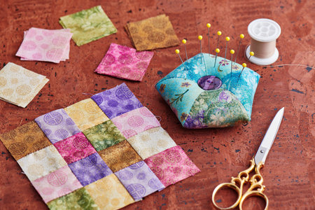 Quilting block from bright square pieces of fabrics, pin cushion, scissors, spool of thread