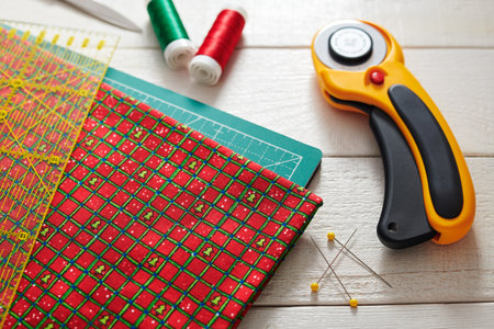 Christmas fabric and ruler on craft mat surrounded quilting and sewing accessoriesの写真素材