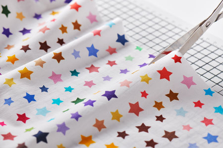 Process cutting fabric with a pattern of colorful stars by scissors on craft matの写真素材
