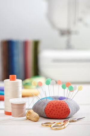 Pin cushion, brightly colored strips of fabric, sewing accessories on the background of stack of...