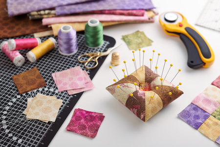 Pin cushion, stacks of square pieces of fabric, pile of patchwork fabrics, quilting and sewing accessoriesの写真素材
