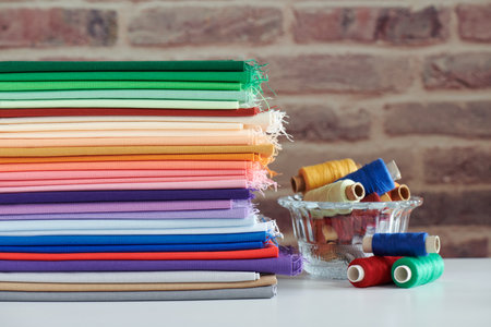 Stack of colorful monochromatic fabrics and spools of thread on brick wall backgroundの写真素材