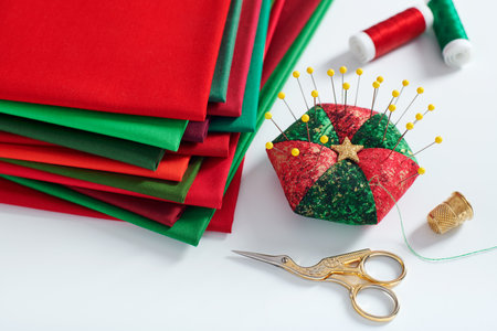 Pile of red and green fabrics, pincushion, scissors, thimble and spools of thread on white backgroundの写真素材