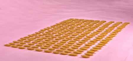 Pasta penne laid out on a white background in even rows.