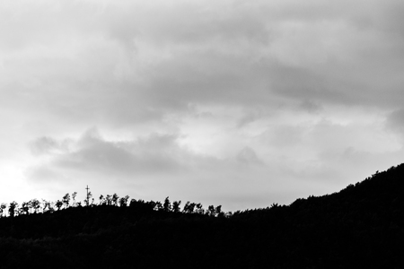 A silhouette of a hill peak at sunset, beneath sun rays coming out through some cloudsの写真素材