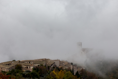 View of St. Francis papal church in Assisi (Umbria, Italy) in the middle of lifting morning fogの写真素材