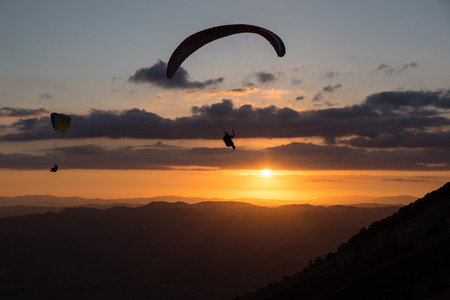 Beautiful shot of two paraglider silhouettes flying over Monte Cucco (Umbria, Italy) with sunset on the background, with beautiful colors and dark tonesの写真素材