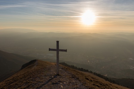 Cross on top of Mt. Serrasanta (Umbria, Italy), with warm golden hour colors and sun low on the horizonの写真素材