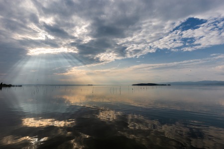 Perfectly symmetric and spectacular view of a lake, with clouds, sky and sun rays reflecting on waterの写真素材