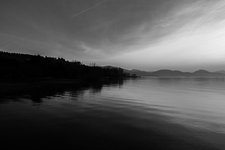 Beautiful view of Trasimeno lake (Umbria, Italy), with hills and sky reflecting on waterの写真素材