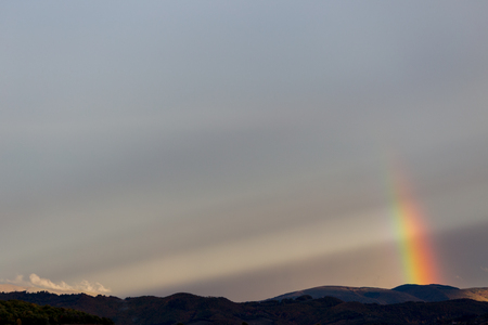 Beautiful and surreal view of part of a rainbow over some hillsの写真素材
