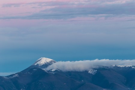 Mountain top covered by snow at sunset, with warm, purple shades reflectionsの写真素材