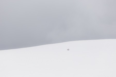 A very minimalistic view of two distant people over a mountain covered by snowの写真素材
