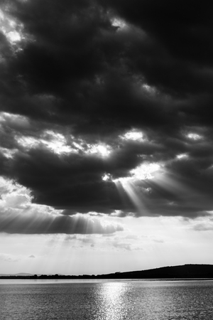 Beautiful sunset on a lake, with sunrays coming down under an overcast skyの写真素材