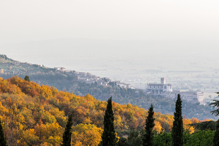 Beautiful view of Assisi town (Umbria) and St.Francis church in autumn from an unusual place, behind an hill with orange and yellow treesの写真素材