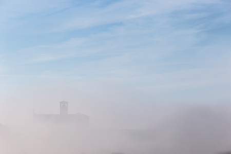 A view of a silhouette of St.Francis church in Assisi in the middle of mist beneath a blue sky with cloudsの写真素材