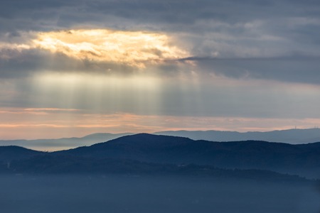 Sunray shines through clouds over the mountains and a sea of fogの写真素材