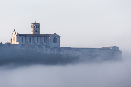 A view of St.Francis church in Assisi in the middle of mist beneath a blue sky with cloudsの写真素材