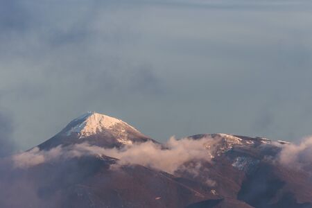 Mountain top covered by snow in the middle of clouds.